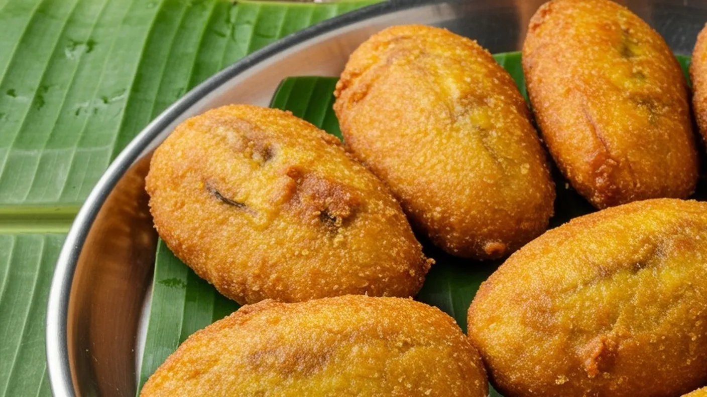 Golden brown pazham pori banana fritters in a crisp batter coating, piled on a banana leaf in a steel plate